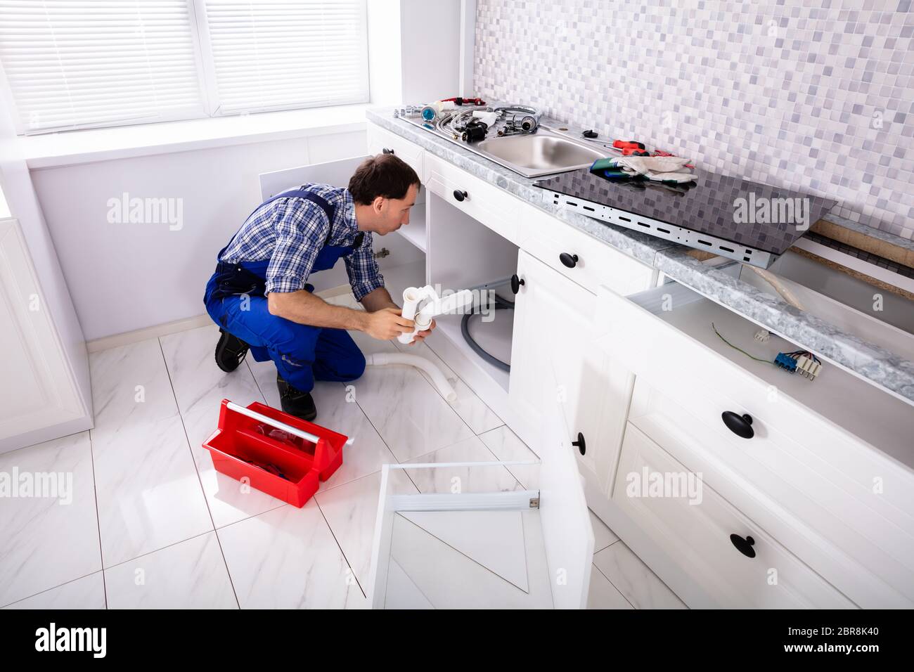 An Overhead View Of Male Plumber Installing Sink Siphon In Domestic Kitchen Stock Photo