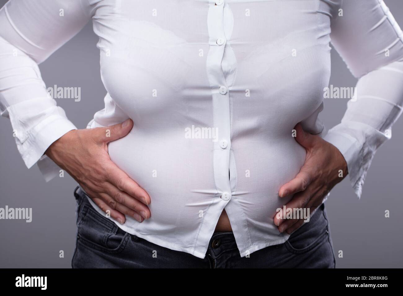 Mid Section Of Fat Woman With Shirt Too Small Touching Her Belly Against Grey Background Stock Photo