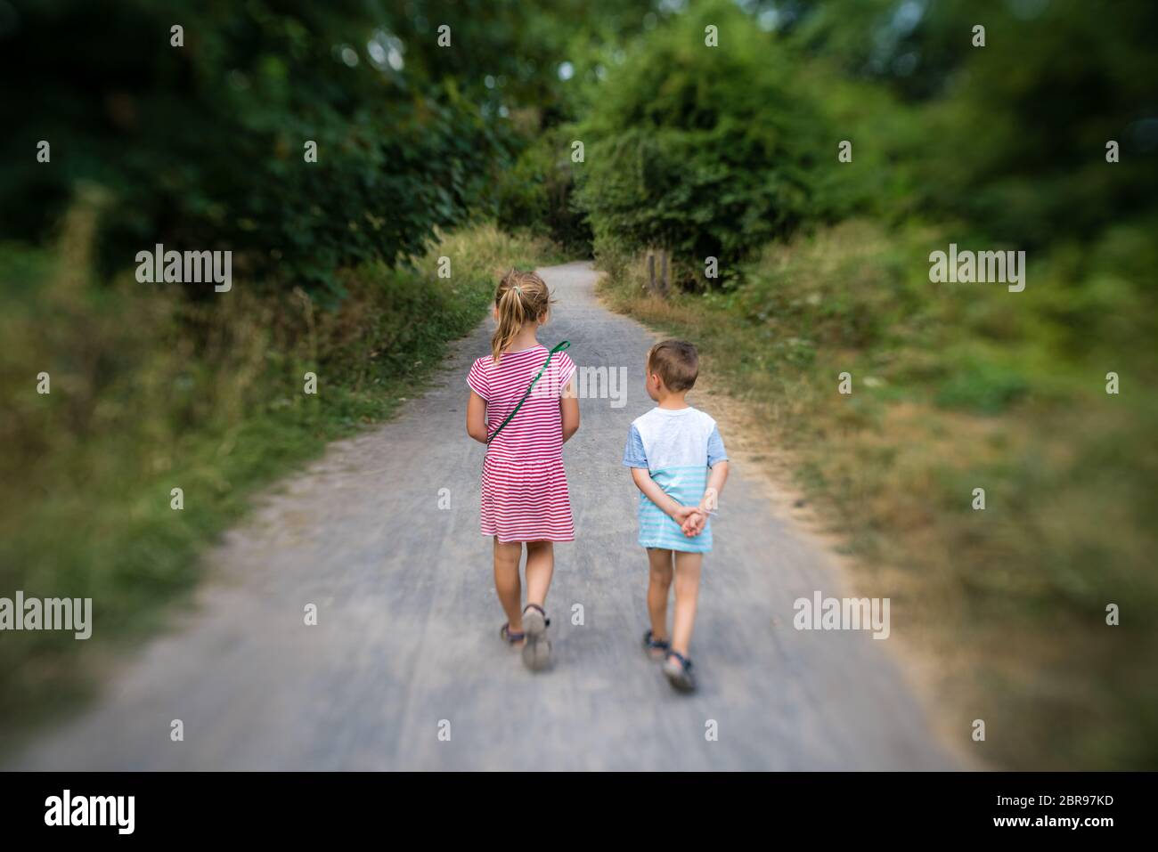 Brother and sister walking together on a narrow paved path in the ...