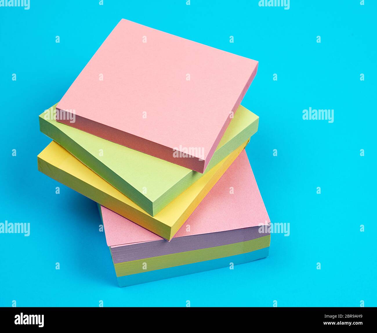 stack of multicolored empty paper square stickers on a blue background, close up Stock Photo