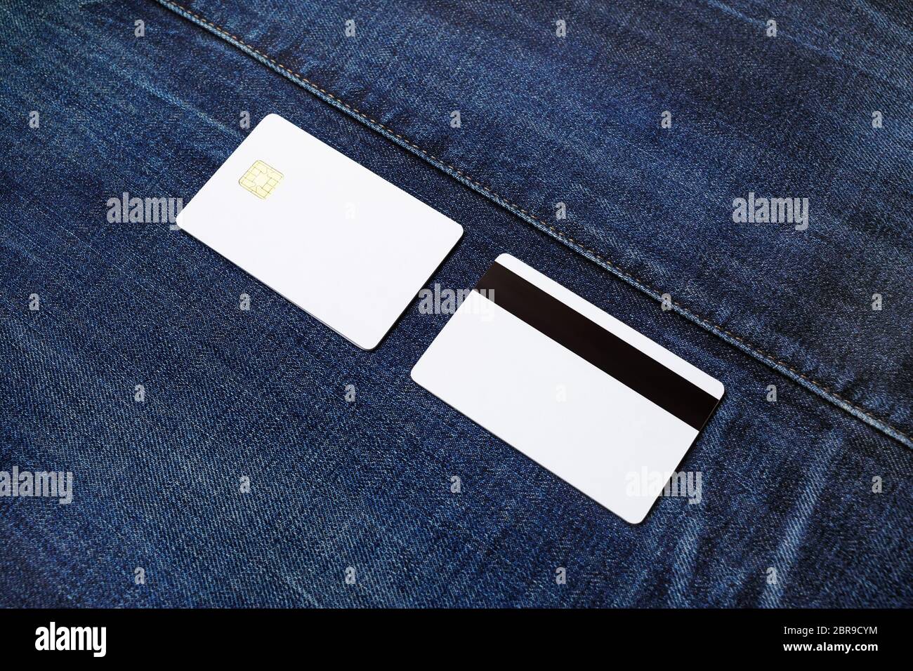 White plastic credit cards on denim background. Front and back view. Stock Photo
