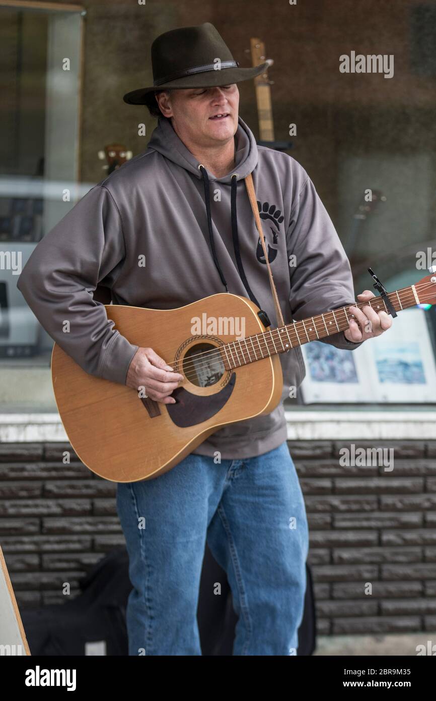 Cowboy singer, playing acoustic guitar, busking on the street, on a sunny day. Stock Photo
