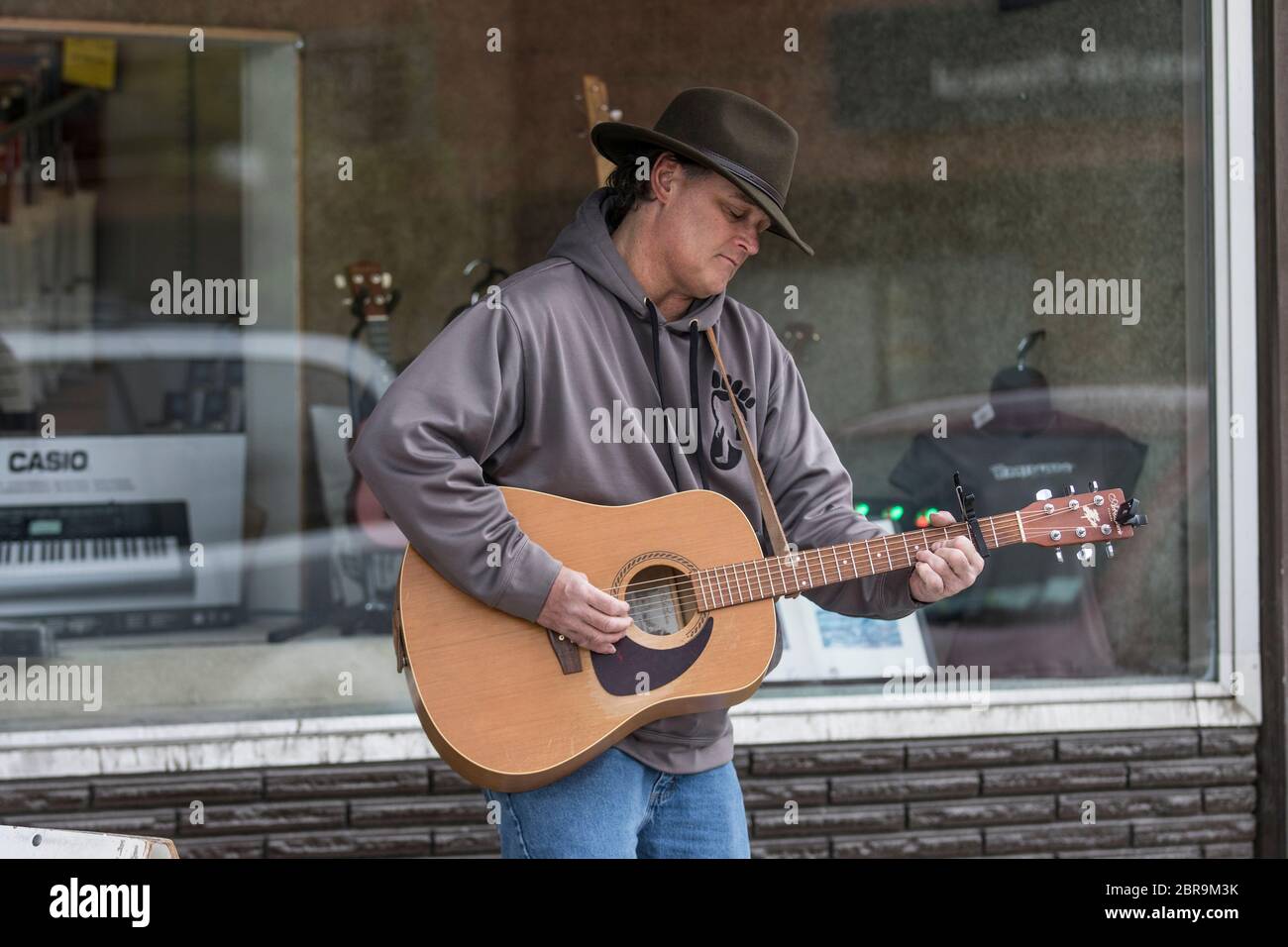 Cowboy singer, playing acoustic guitar, busking on the street, on a sunny day. Stock Photo