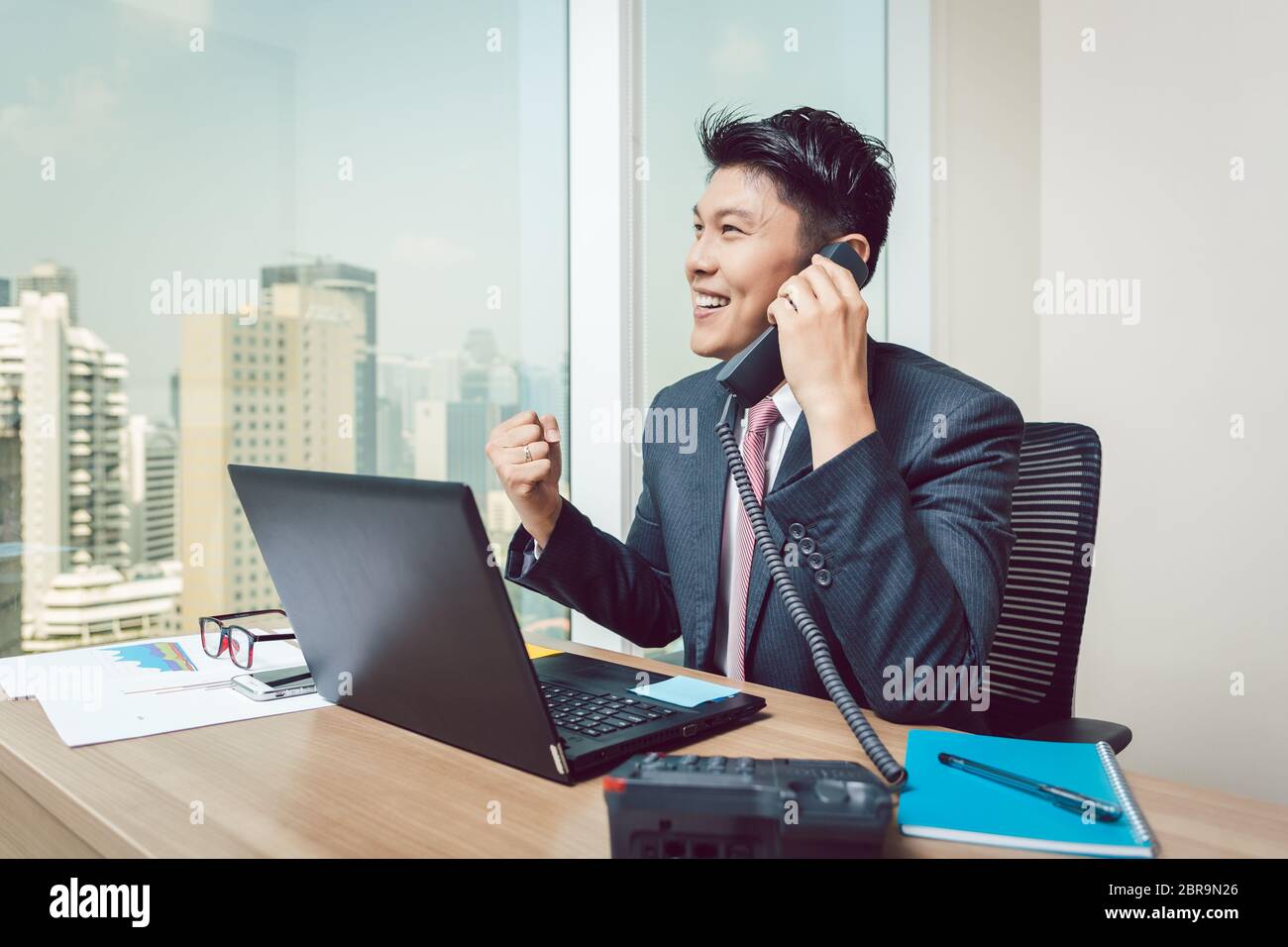 Portrait of successful smiling young businessman talking on telephone clenching his fist Stock Photo