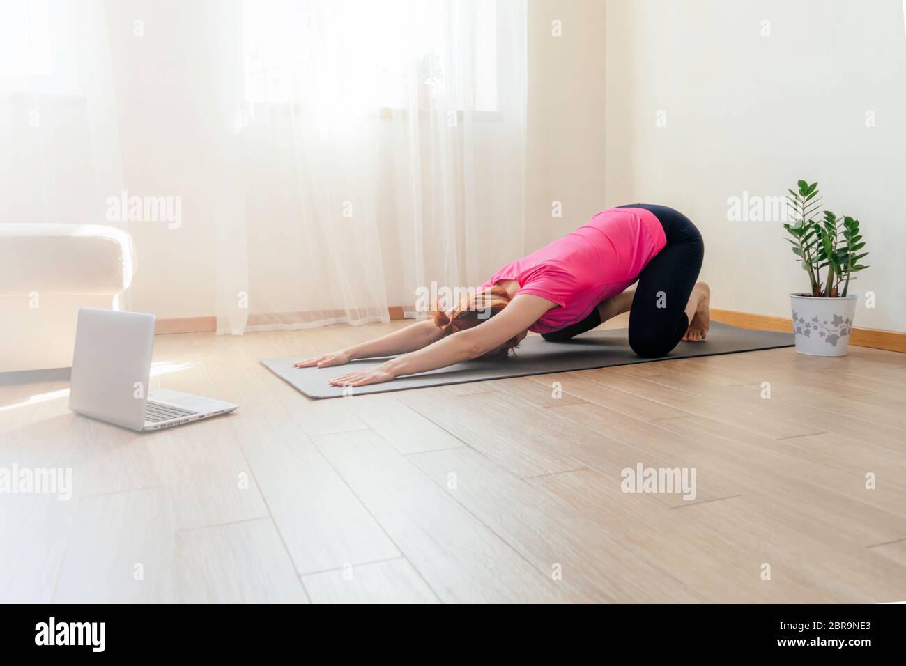 Young woman training on floor at home, doing plank and watching videos on laptop. Yoga, pilates, working out exercising. Quarantine at home. Stock Photo