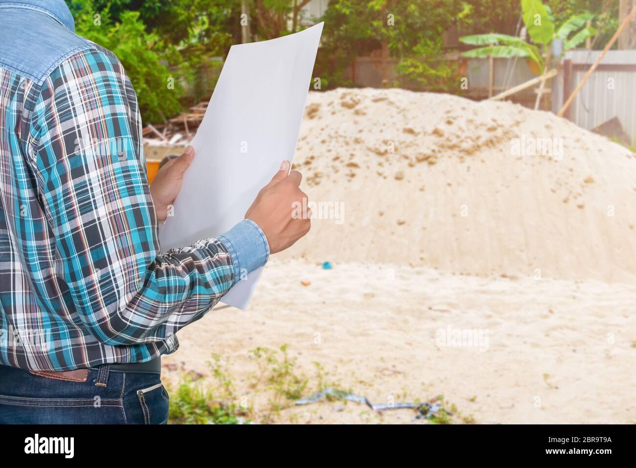 hand engineer holding rolled blueprints and wear white safety helmet plastic in inspect construction site Stock Photo