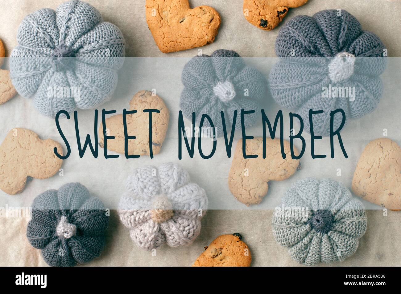 SWEET NIVEMBER text, Autumn still life from handcrafted knitted pumpkin, cookies in heart shape on baking paper. Concept warm cozy home fall season co Stock Photo