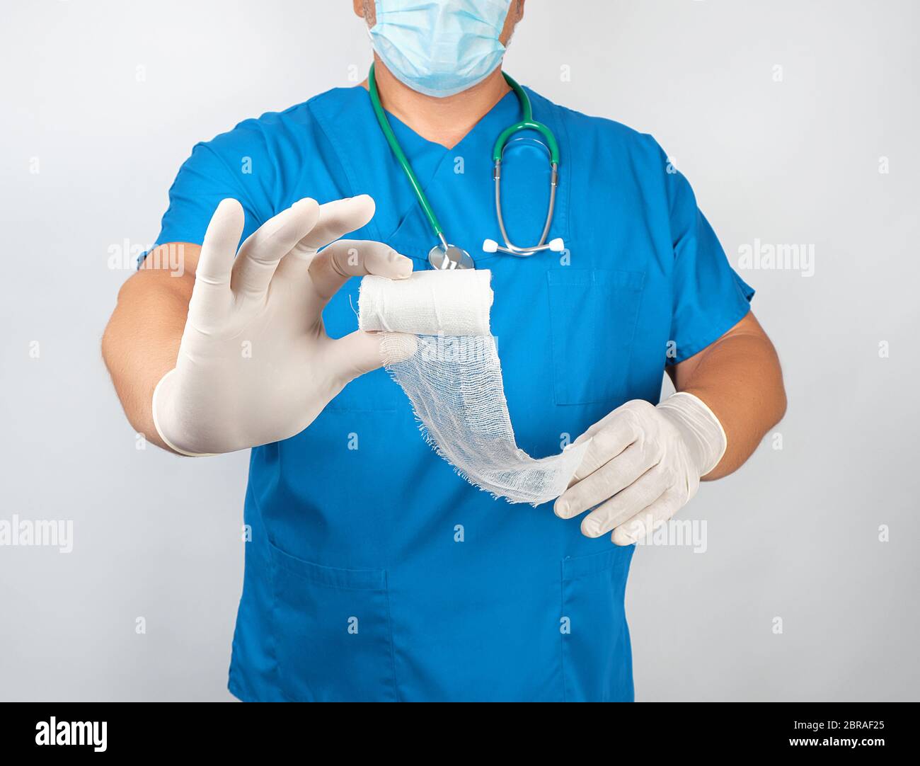 male doctor in blue uniform and latex gloves holding white sterile gauze  dressing bandage, white background Stock Photo - Alamy