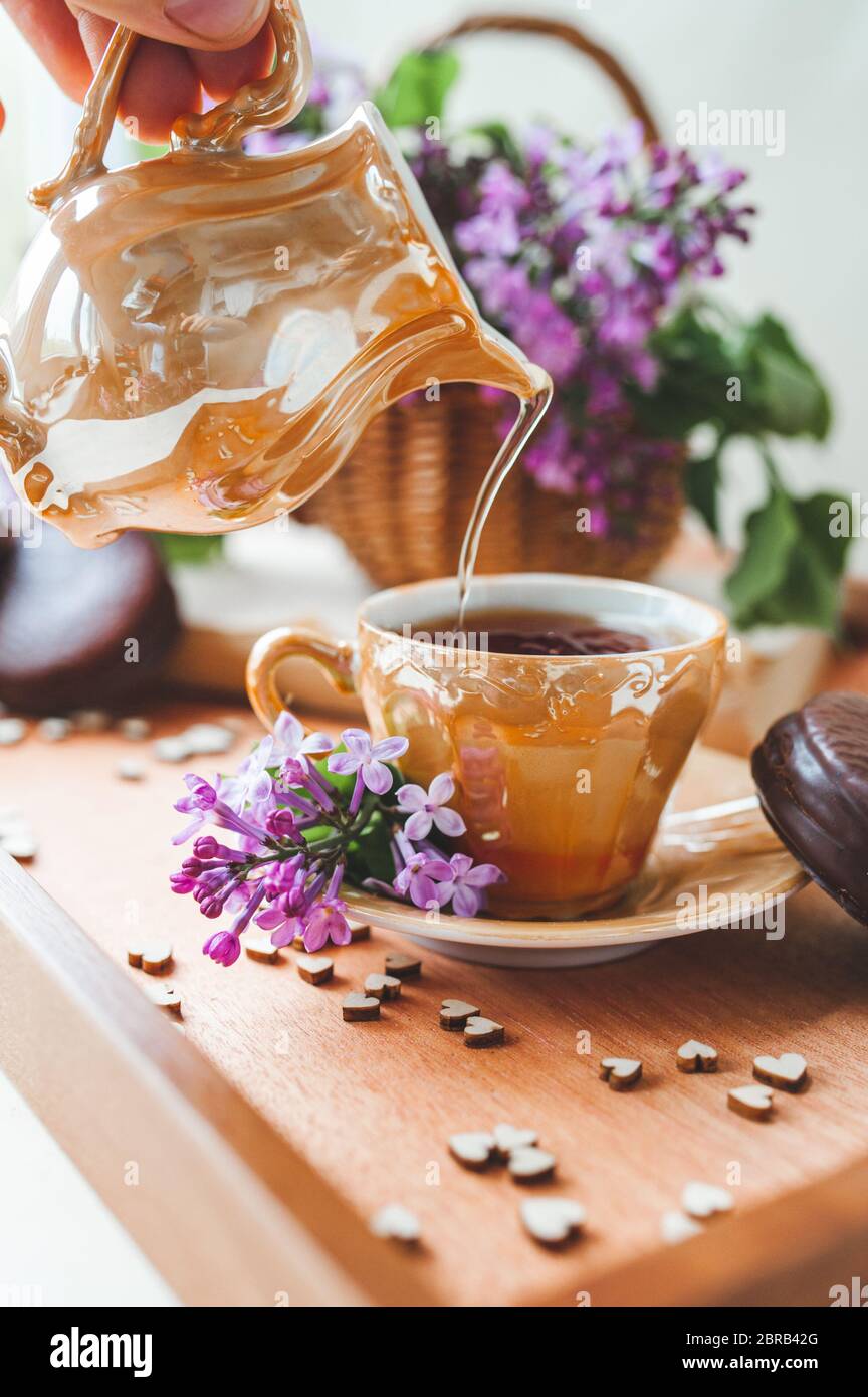 Golden porcelain teapot pours a stream of tea into Cup on wooden tray