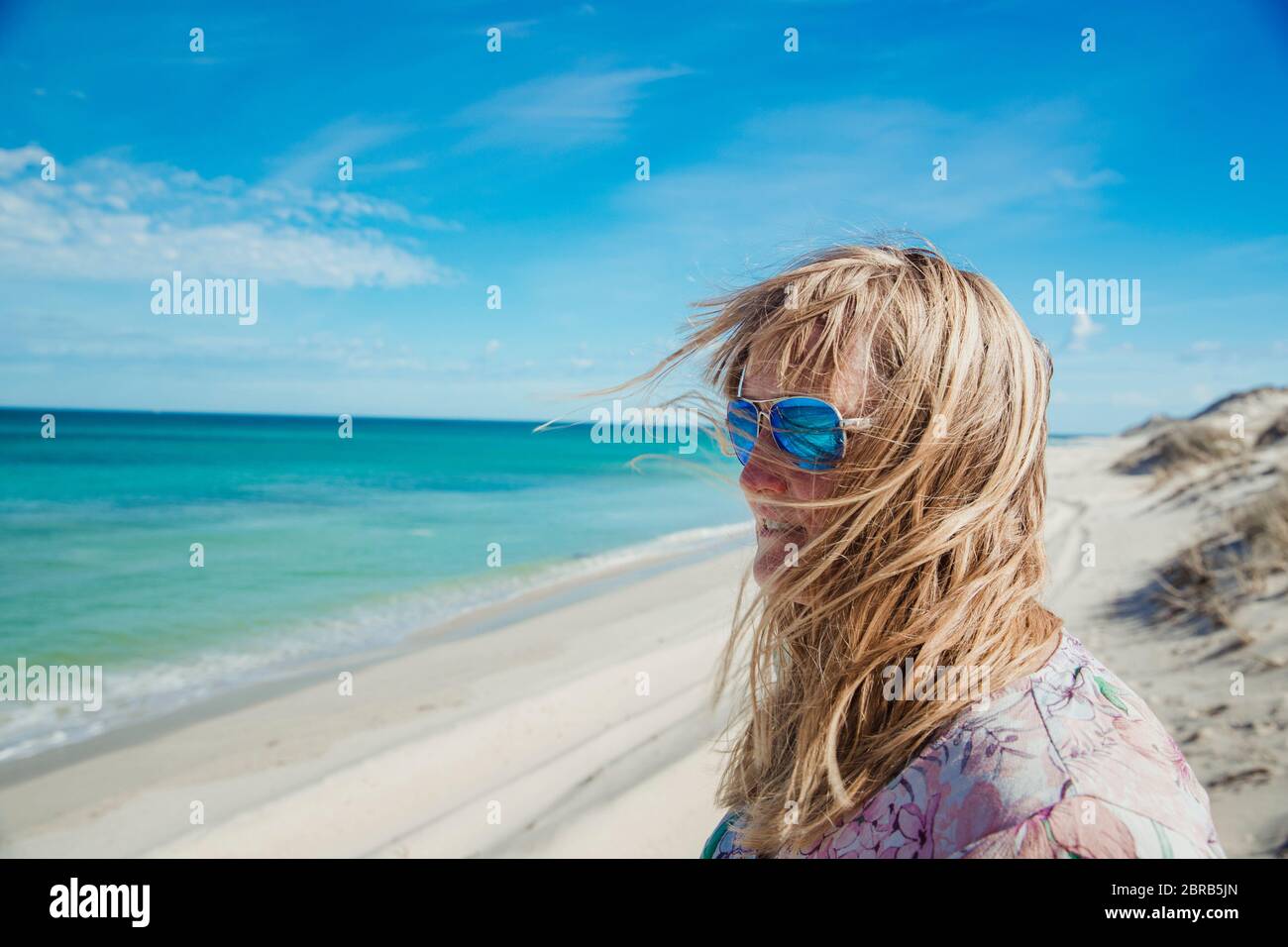 Side view of a mature woman standing and admiring the view from the sand dunes. Her hair is blowing into her face do to the wind. Stock Photo