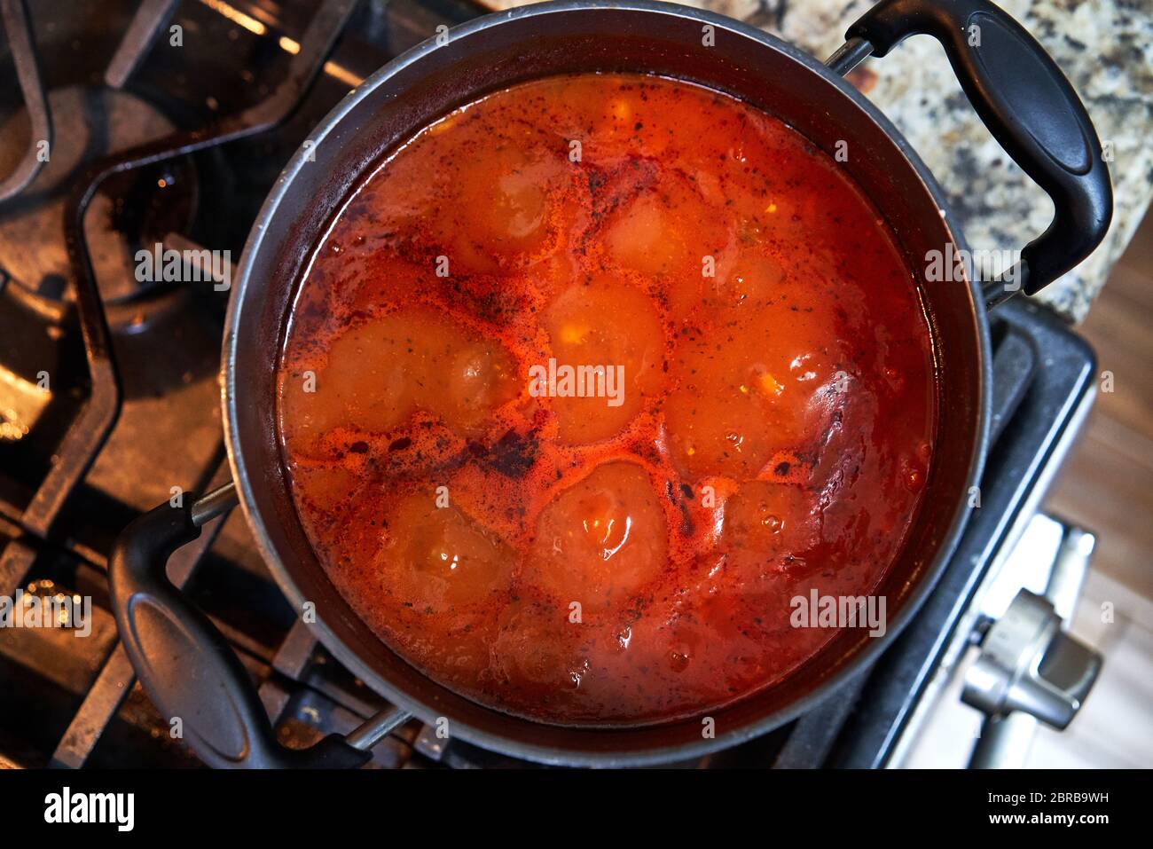 Overhead view of red tomato soup in a pot cooking on the stove in a kitchen. Stock Photo