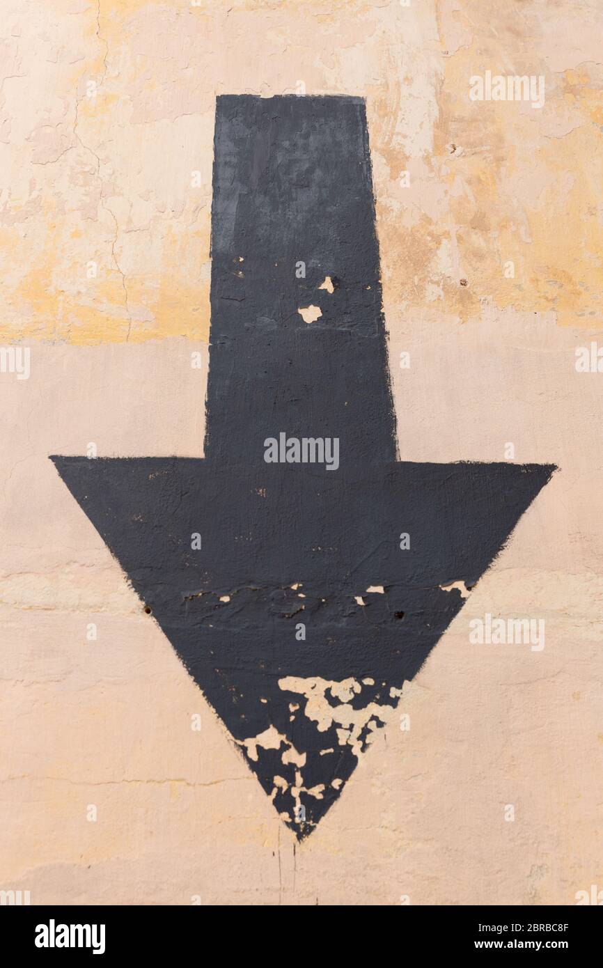 Black aged arrow on concrete wall pointing down Stock Photo