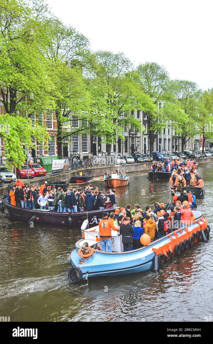 Amsterdam, Netherlands - April 27, 2019: Party boats with people dressed in national orange color while celebrating the Kings day, Koningsdag, the birthday of the Dutch King Willem-Alexander. Stock Photo