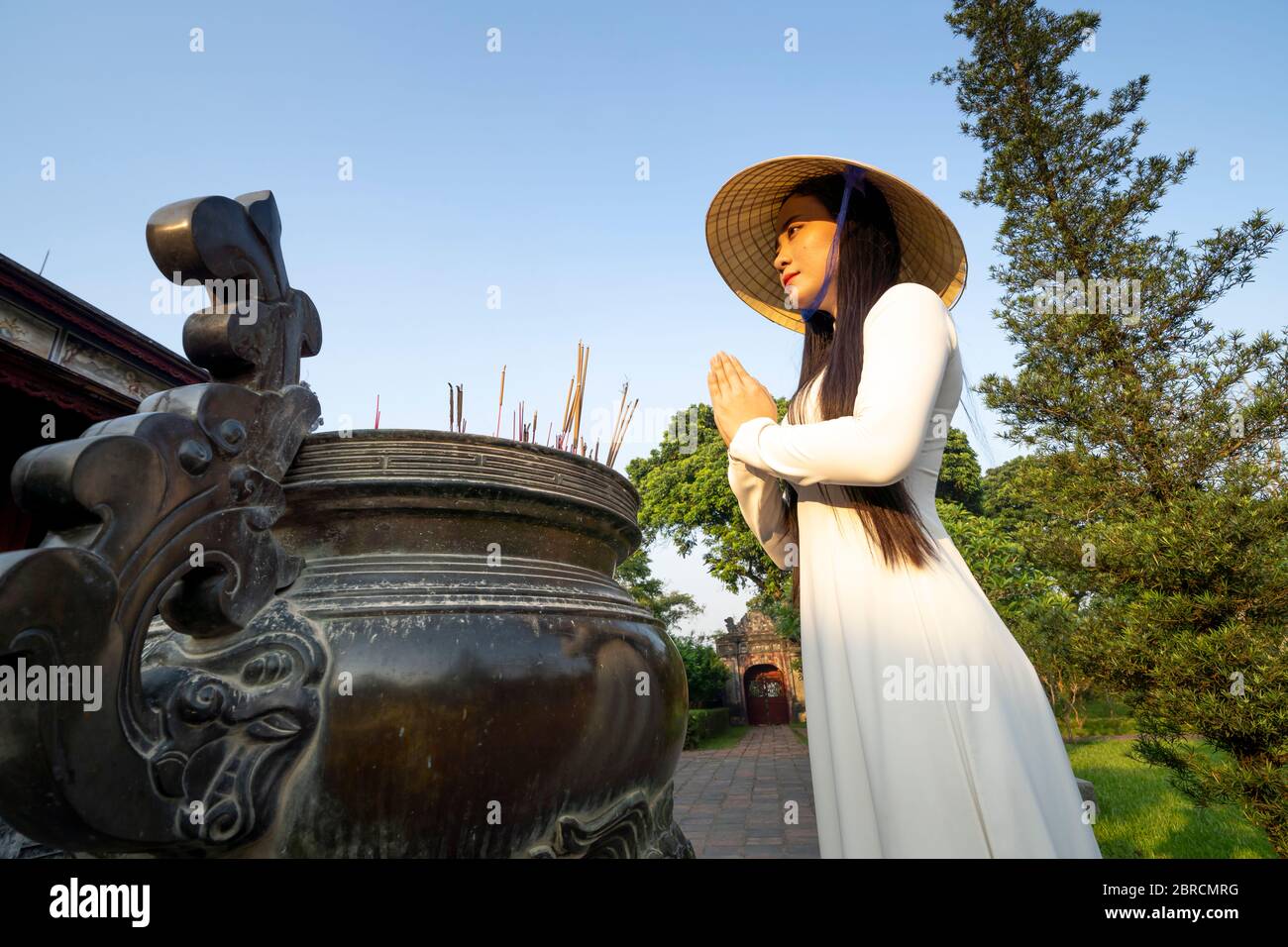Hue City, Thua Thien Hue Province, Vietnam - May 7, 2020: A scene of a girl in a traditional ao dai costume praying inside a temple Stock Photo