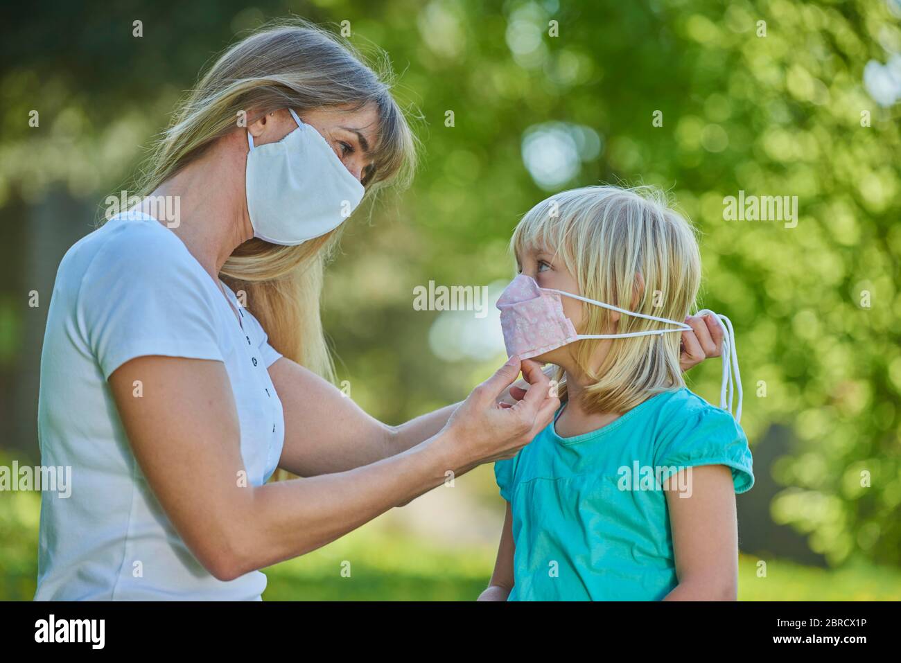 Mutter legt Tochter Mundschutzmaske an, Stadtpark, Corona-Krise, Regensburg, Bayern, Deutschland Stock Photo