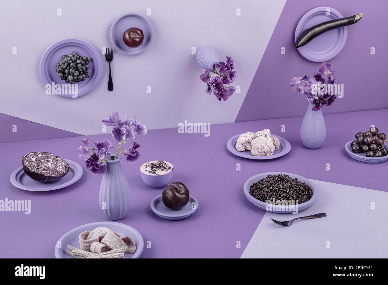 Laid table in violet, perspective, surreal, eggplant, red cabbage, rice, yogurt, grapes, apple, flowers, cauliflower, still life, food photography Stock Photo