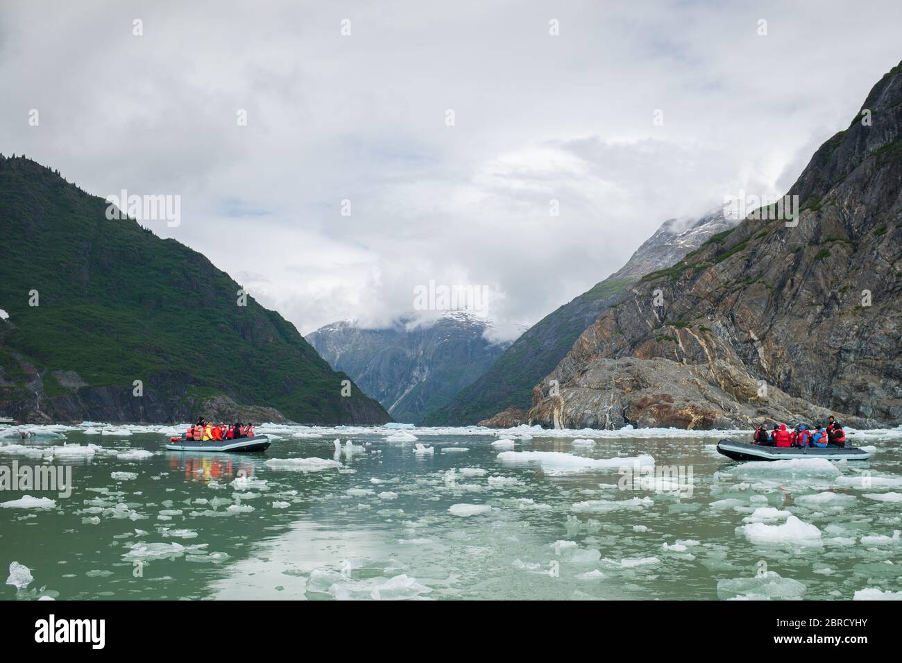 icebergs calved from South Sawyer Glacier float down scenic Tracy Arm Fjord, Southeast Alaska, USA, past adventurous tourists on skiff boats from a sm Stock Photo