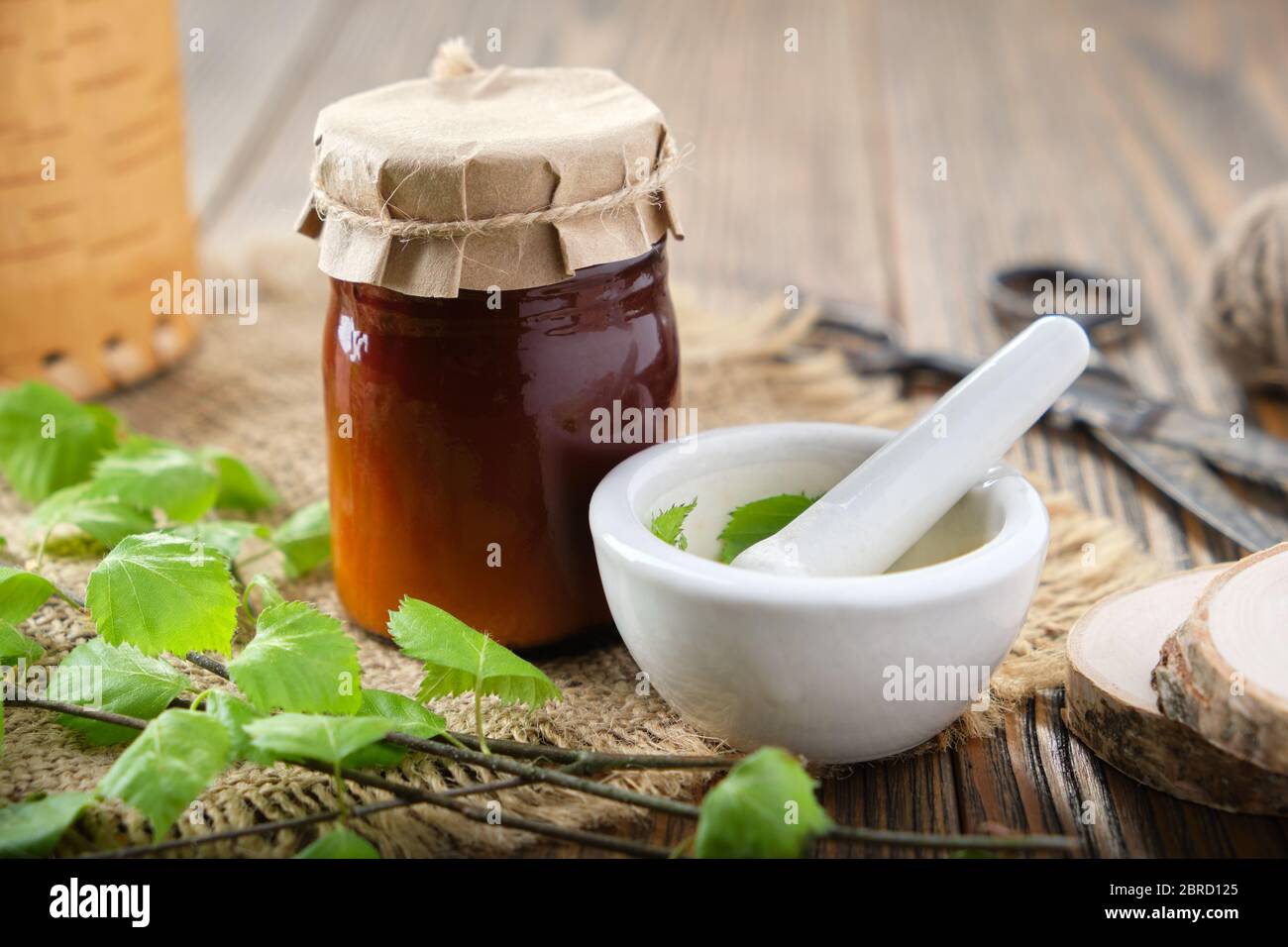 Bottle of birch herbal salve, balm or coal tar oil, healthy birch leaves, mortar on wooden table. Alternative medicine. Stock Photo
