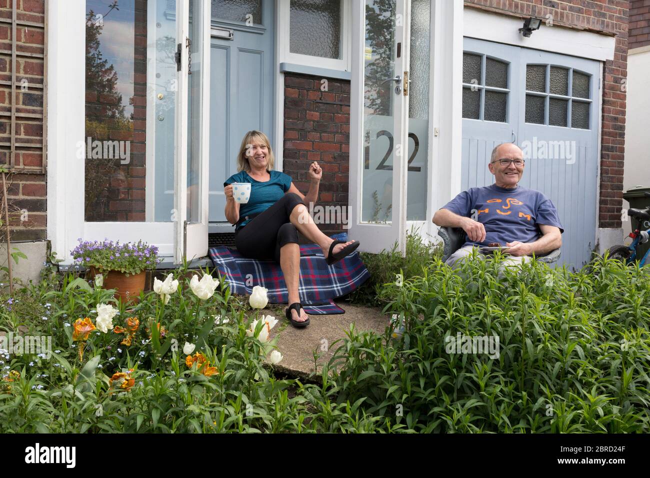 As the country continues the UK government's Coronavirus lockdown with social distancing rules still in effect, a middle-class couple sit on the porch in the front garden outside their home in Herne Hill, south London, on 17th May 2020, in London, England. Stock Photo