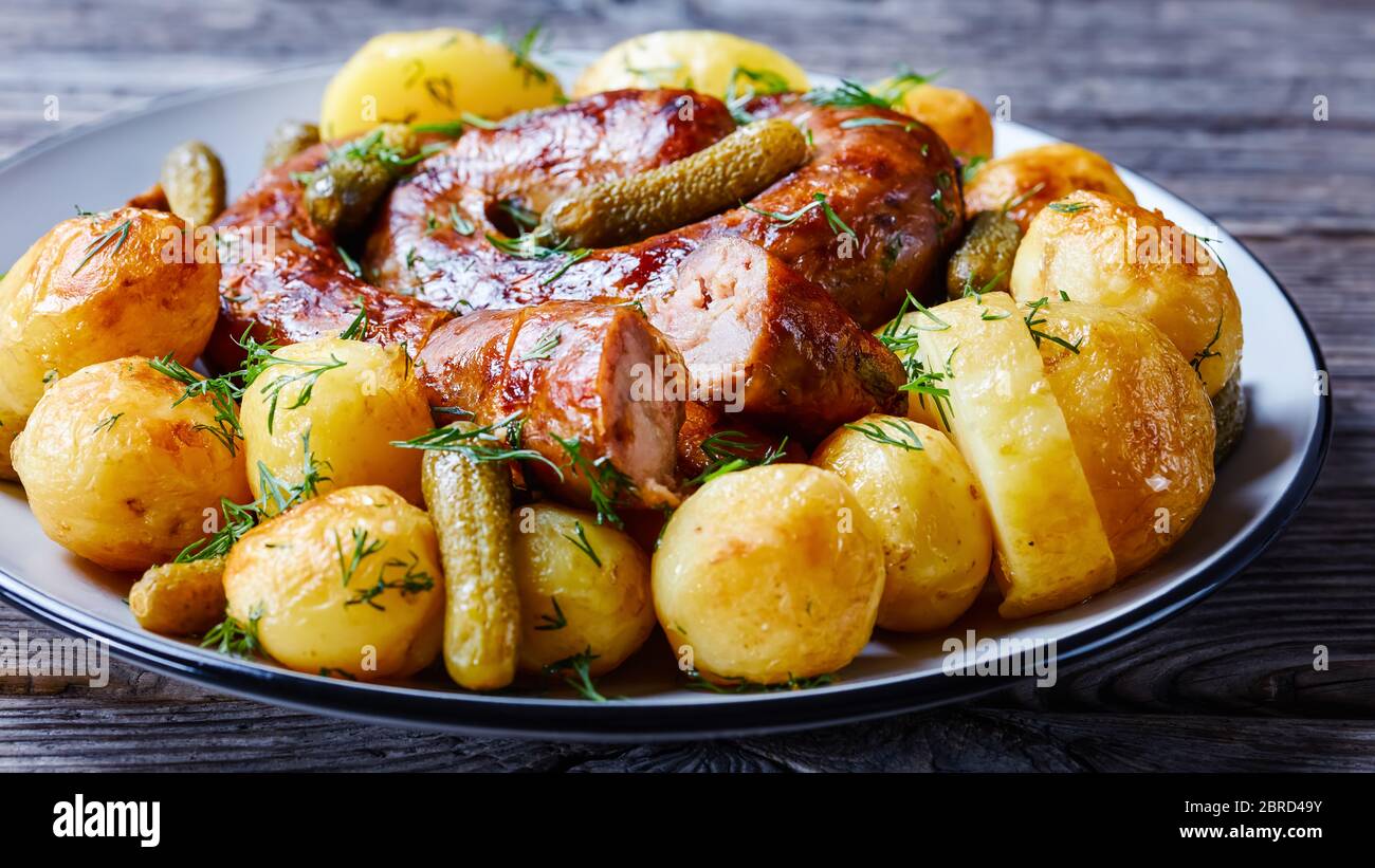 Authentic german spiral sausage with young potato and pickled cucumbers, sprinkled with fresh dill, served on a plate on an old barn wooden background Stock Photo