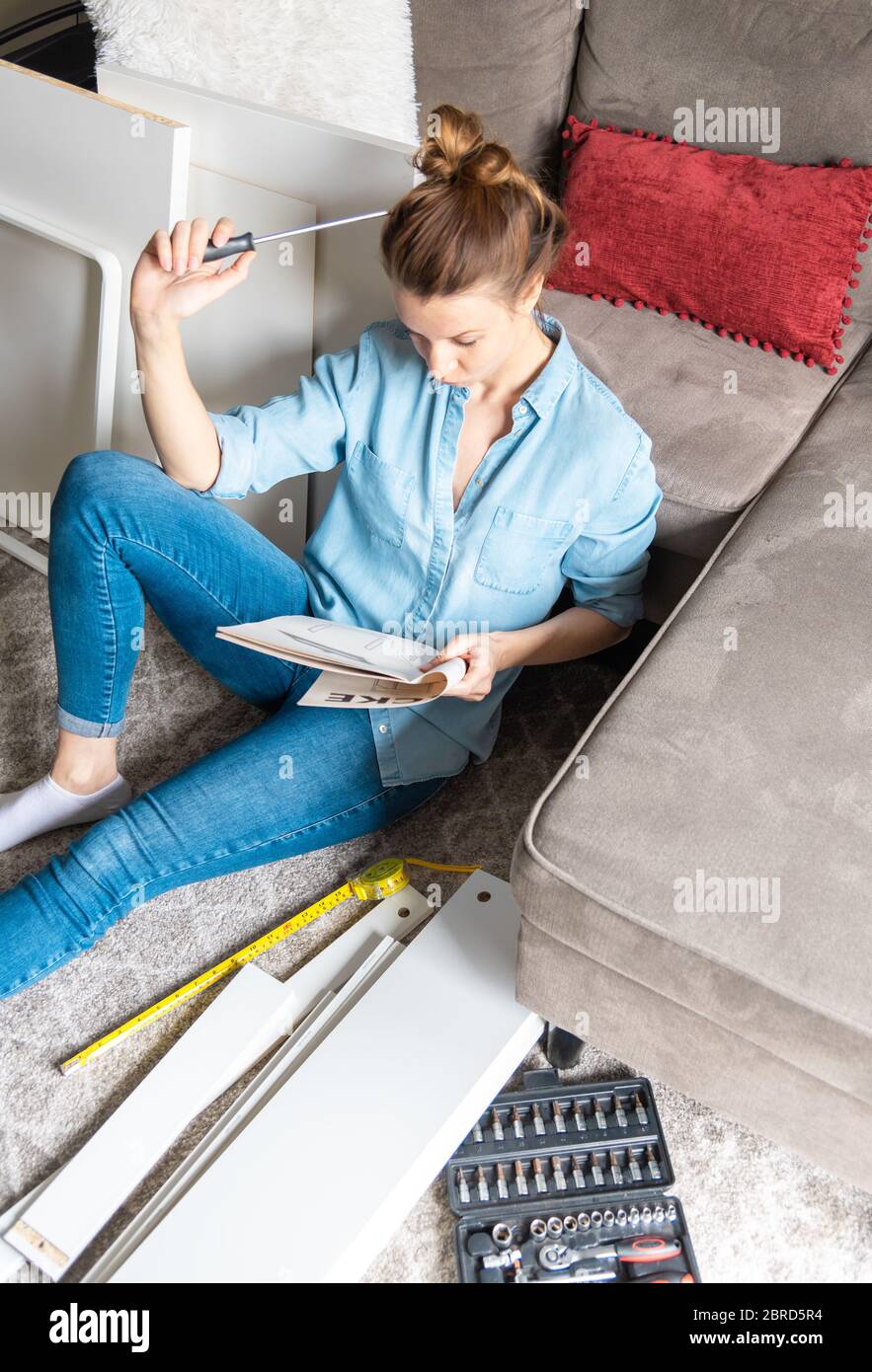 Concentrated young woman reading the instructions to assemble furniture