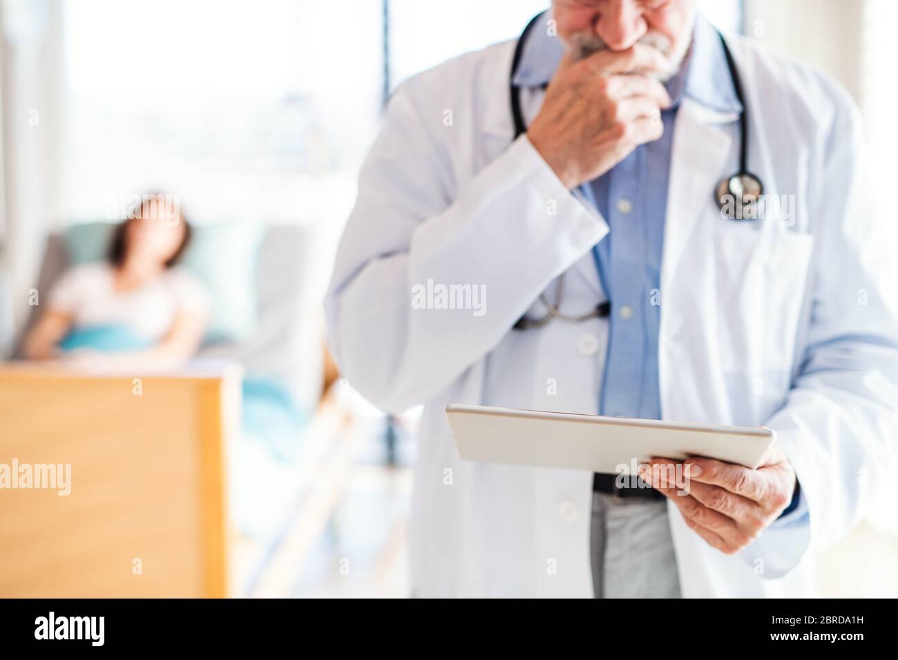 Unrecognizable senior male doctor standing in hospital room, using tablet. Stock Photo