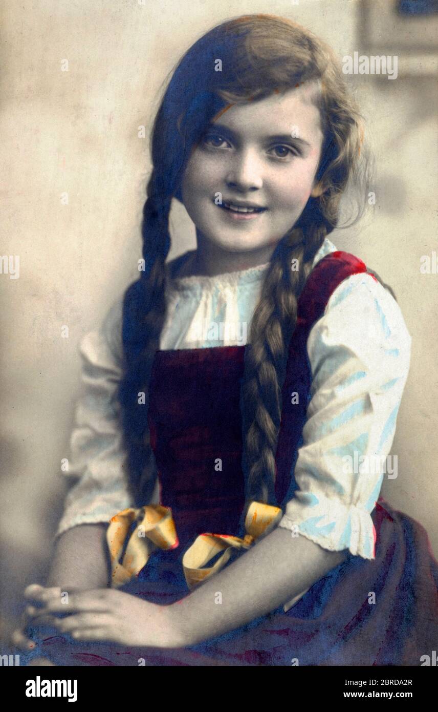 smiling young girl with pigtails poses in studio for a hand tinted portrait 1920s hungary Stock Photo