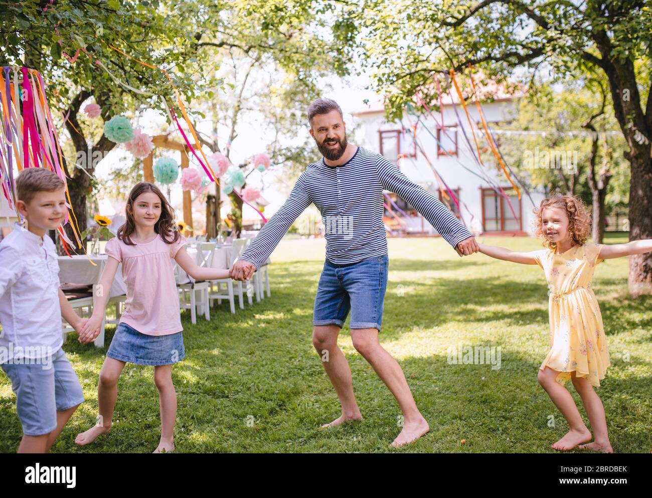 Man with kids on birthday party playing outdoors in garden in summer. Stock Photo