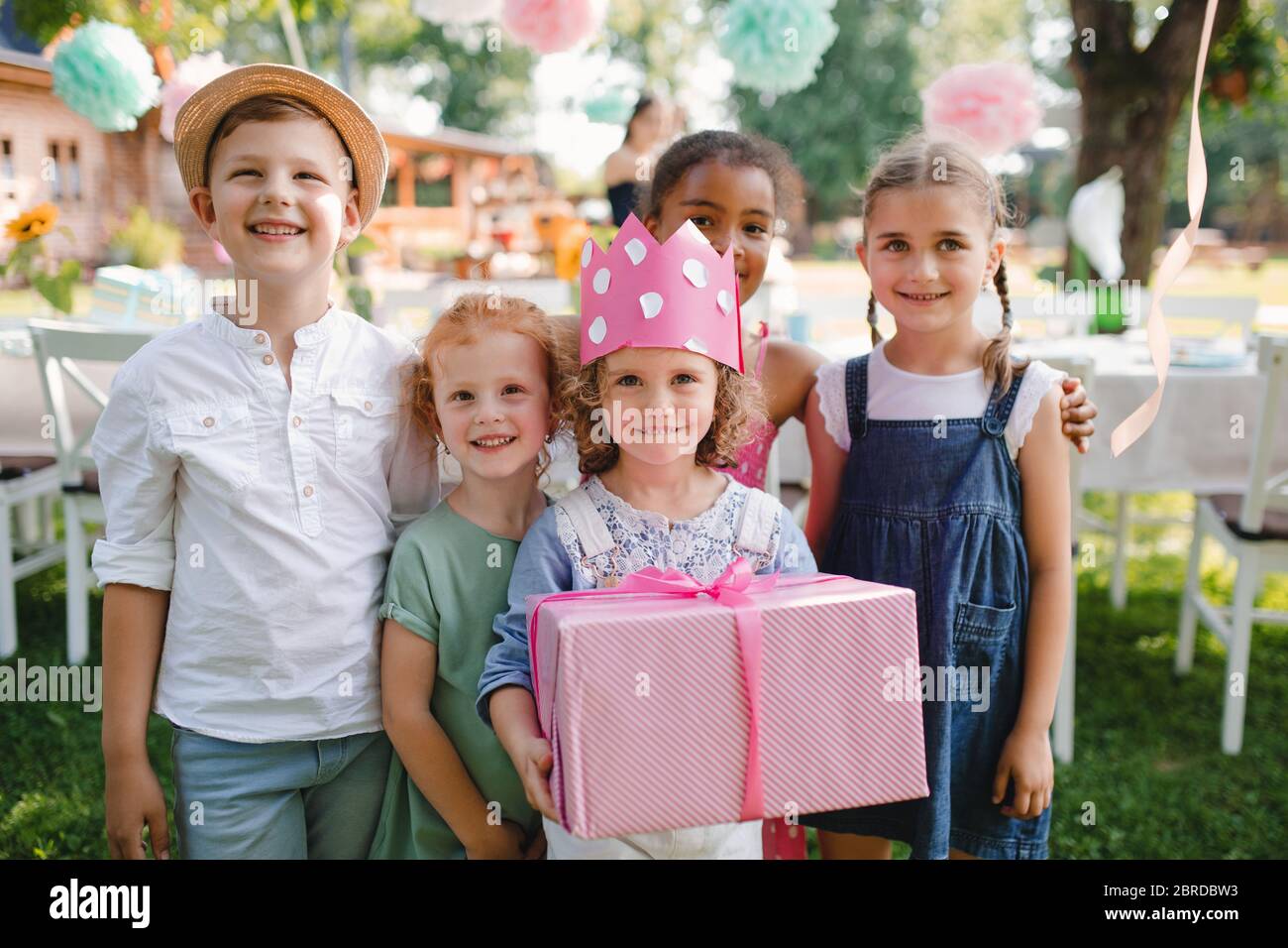 Portrait of small girl with friends and present outdoors in garden in summer. Stock Photo