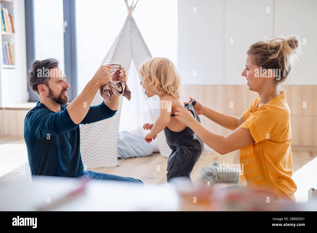 Young family with small child indoors in bedroom getting dressed. Stock Photo