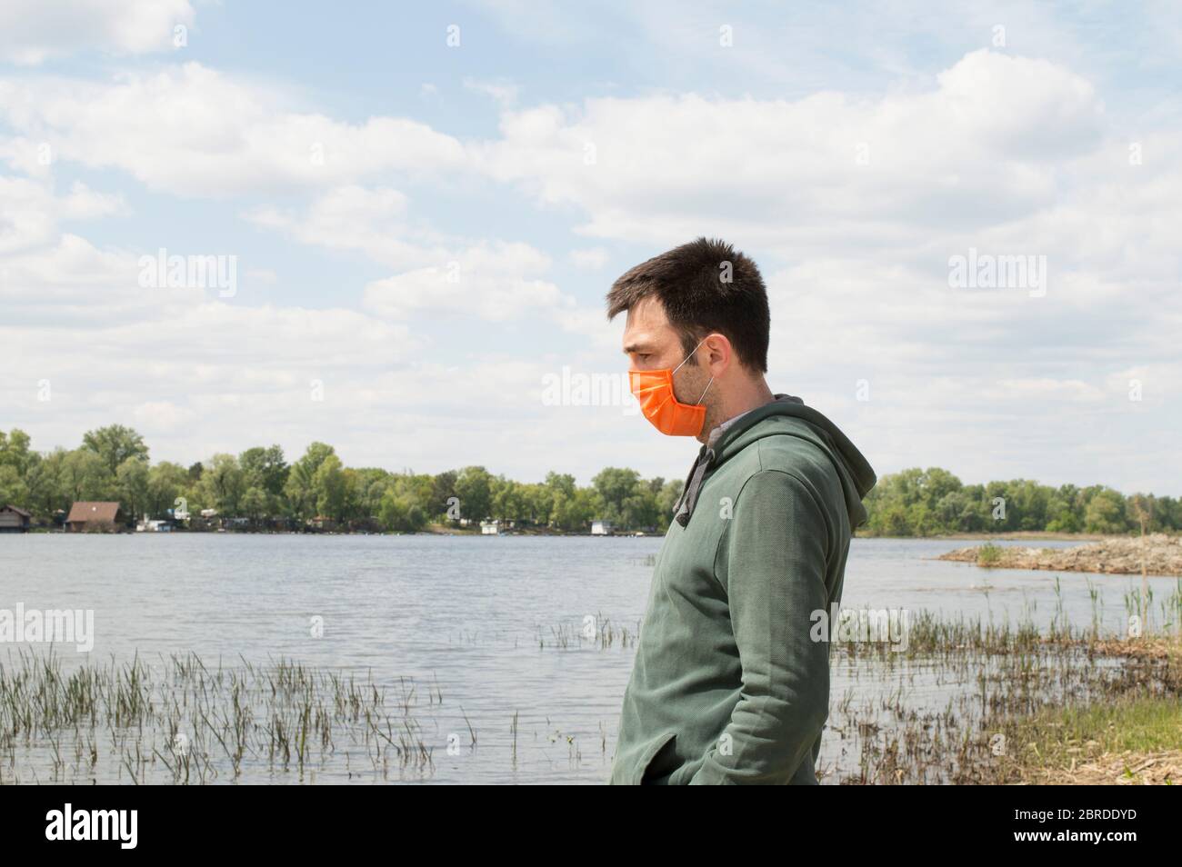 Portrait of Turkish man in profile in green hoodie and bright orange mask is looking to river in Kyiv, Ukraine. Health care protection concepts during Stock Photo