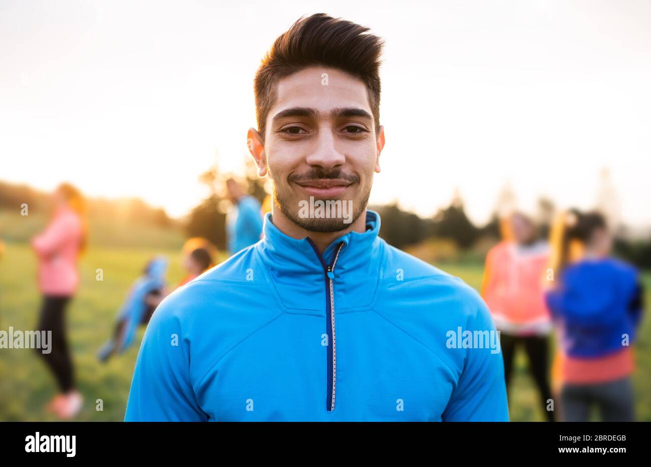 A portrait of young man with large group of people doing exercise in nature. Stock Photo