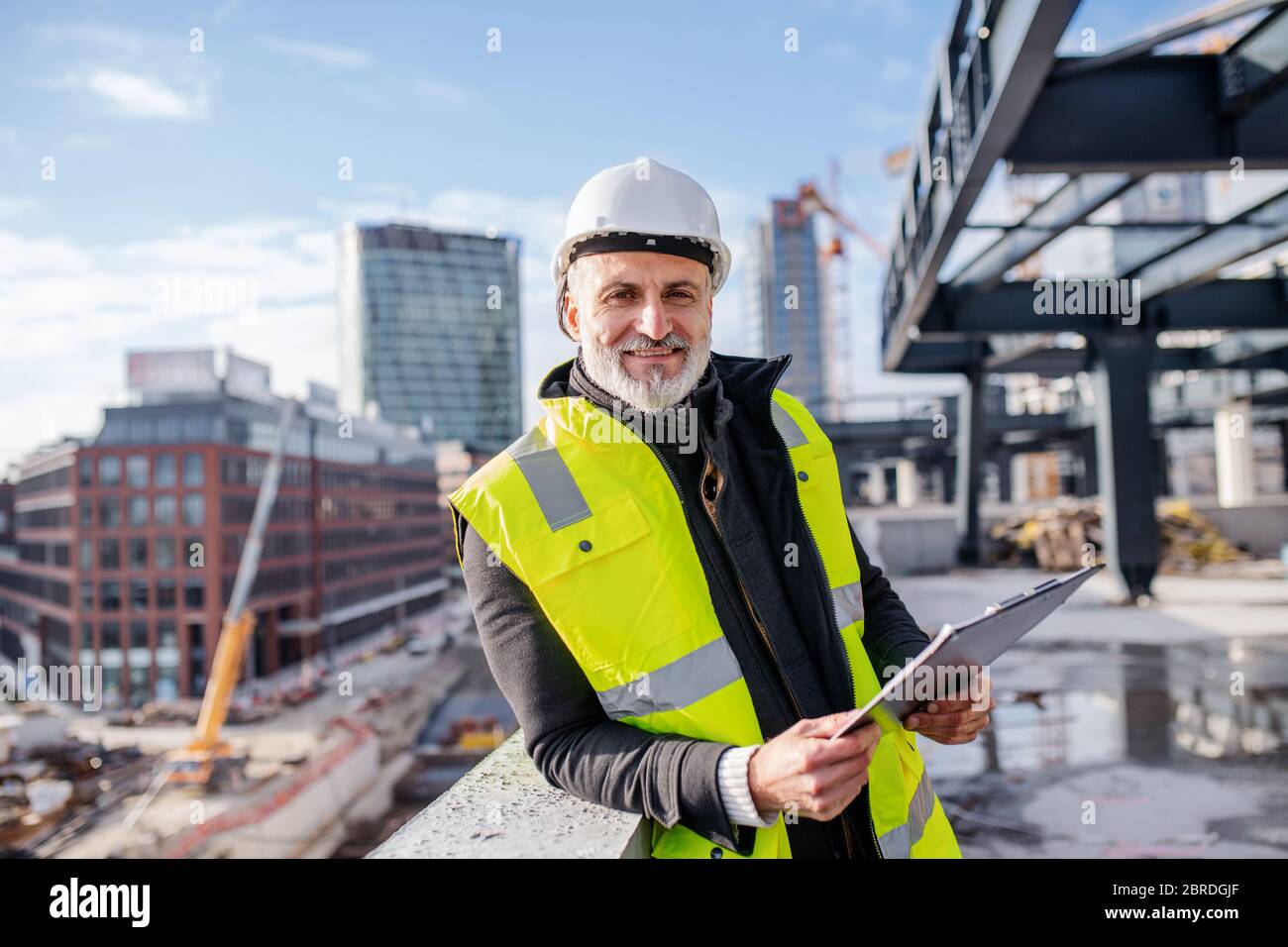 Man engineer standing outdoors on construction site, looking at camera. Stock Photo