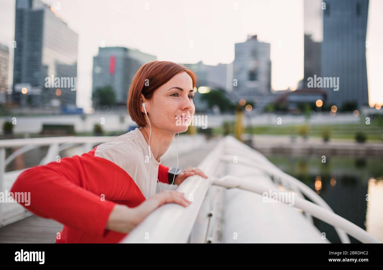 Side view of young woman runner with earphones in city, stretching. Stock Photo