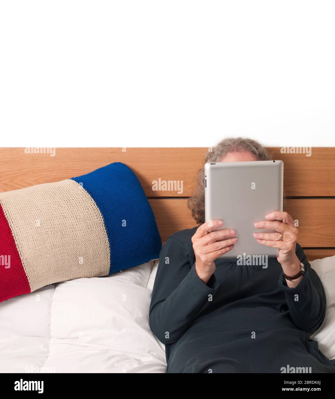 Older woman lying on a bed browsing the internet with a digital tablet beside a French Tricolor flag pillow Stock Photo