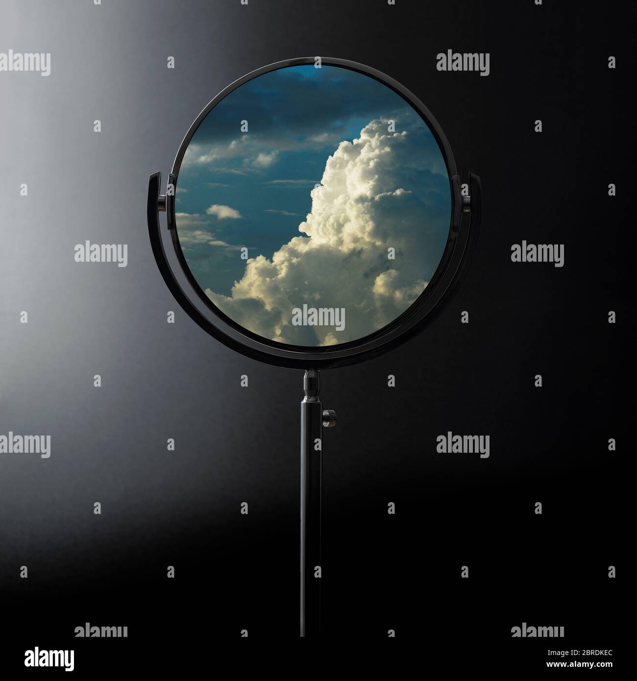 Circular shaving mirror on dark background reflecting clouds Stock Photo