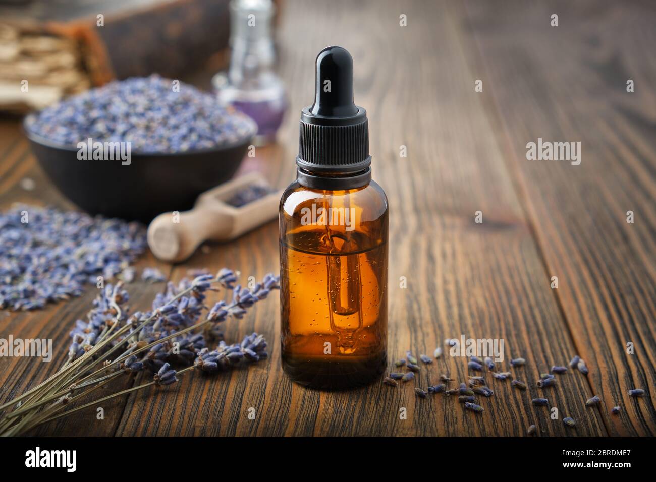 Dropper bottle of essential lavender oil. Bowl of dry lavender flowers on background. Stock Photo