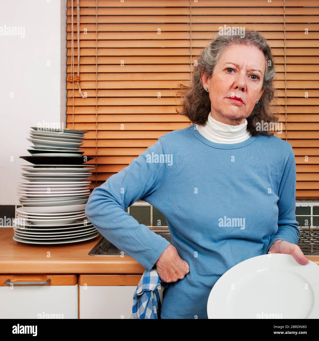 Woman hand washing large pile of plates, looking bored Stock Photo