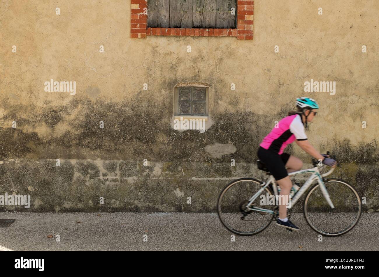 Woman cyclist passing old village house at Rasteau in southern France Stock Photo