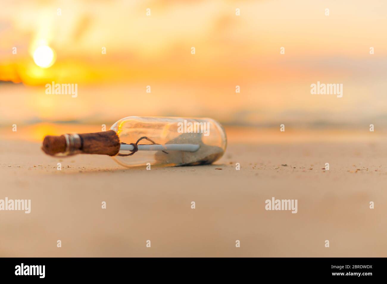 Message in the bottle washed ashore against the sun setting down. Tropical sunset beach design background. Castaway, loneliness, lost concept Stock Photo