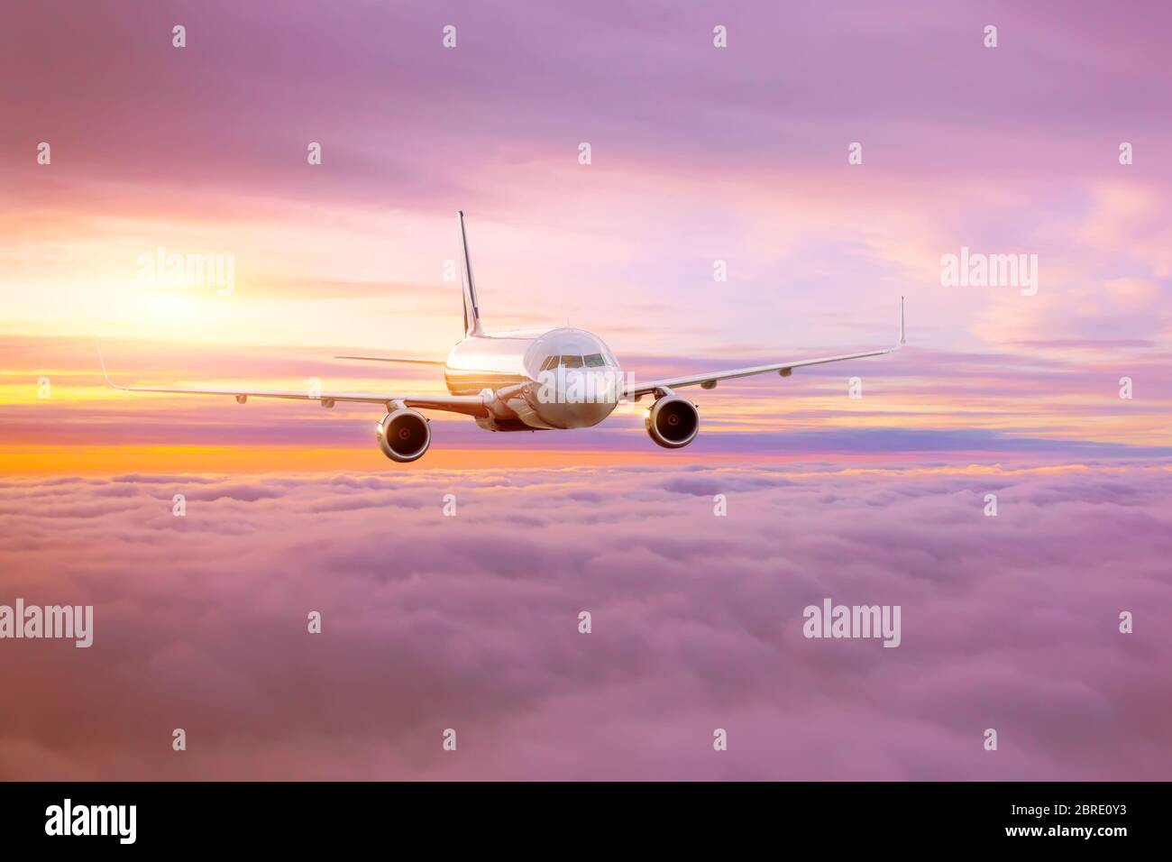 Passenger airplane in the morning sun flies high above the pink-tinted clouds with glare on the fuselage Stock Photo