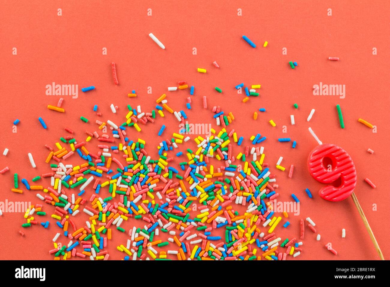 Nine year old cake candle number and birthday cake sprinkles on bright orange background - top view Stock Photo