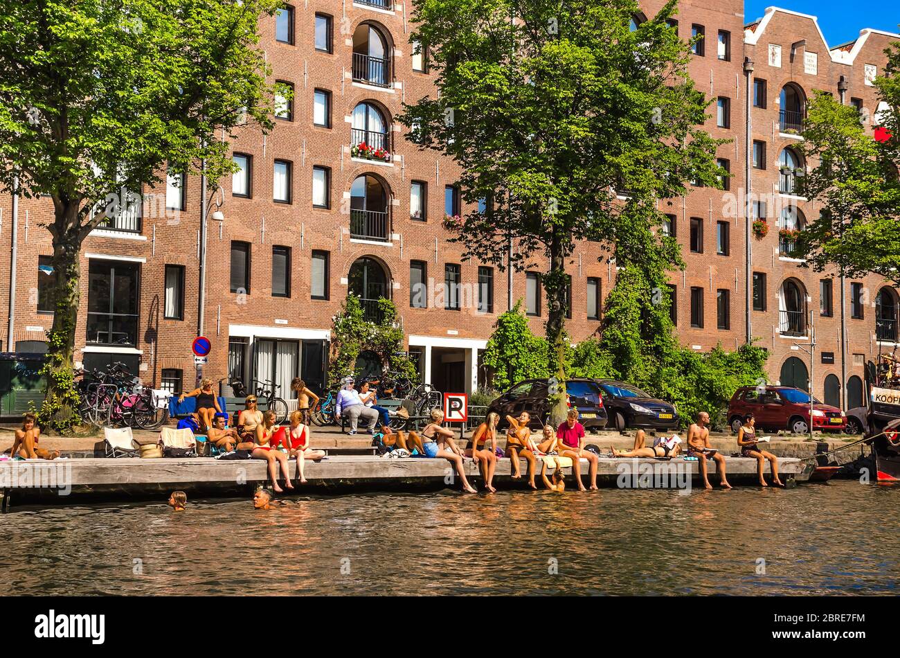 AMSTERDAM, HOLLAND – AUG. 31, 2019: Tourists and happy families relaxing and enjoying summer vacation on sunny days at Amstel river (city canal). Stock Photo