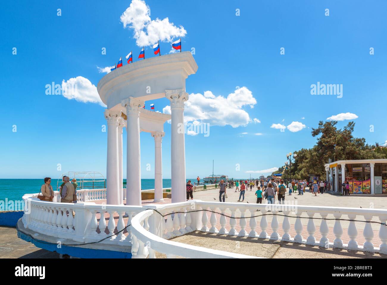 ALUSHTA, CRIMEA - MAY 15, 2016: People visit the urban beach in Crimea, Russia. Scenic view of the Black Sea waterfront in Crimea. White colonnade wit Stock Photo