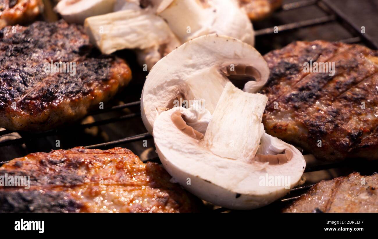 Beef BBQ Cooking of burger meat and mushroom. Iron barbeque grill pan with fire and food. Hamburgers outdoors barbecuing on coals. Closeup beef. Stock Photo