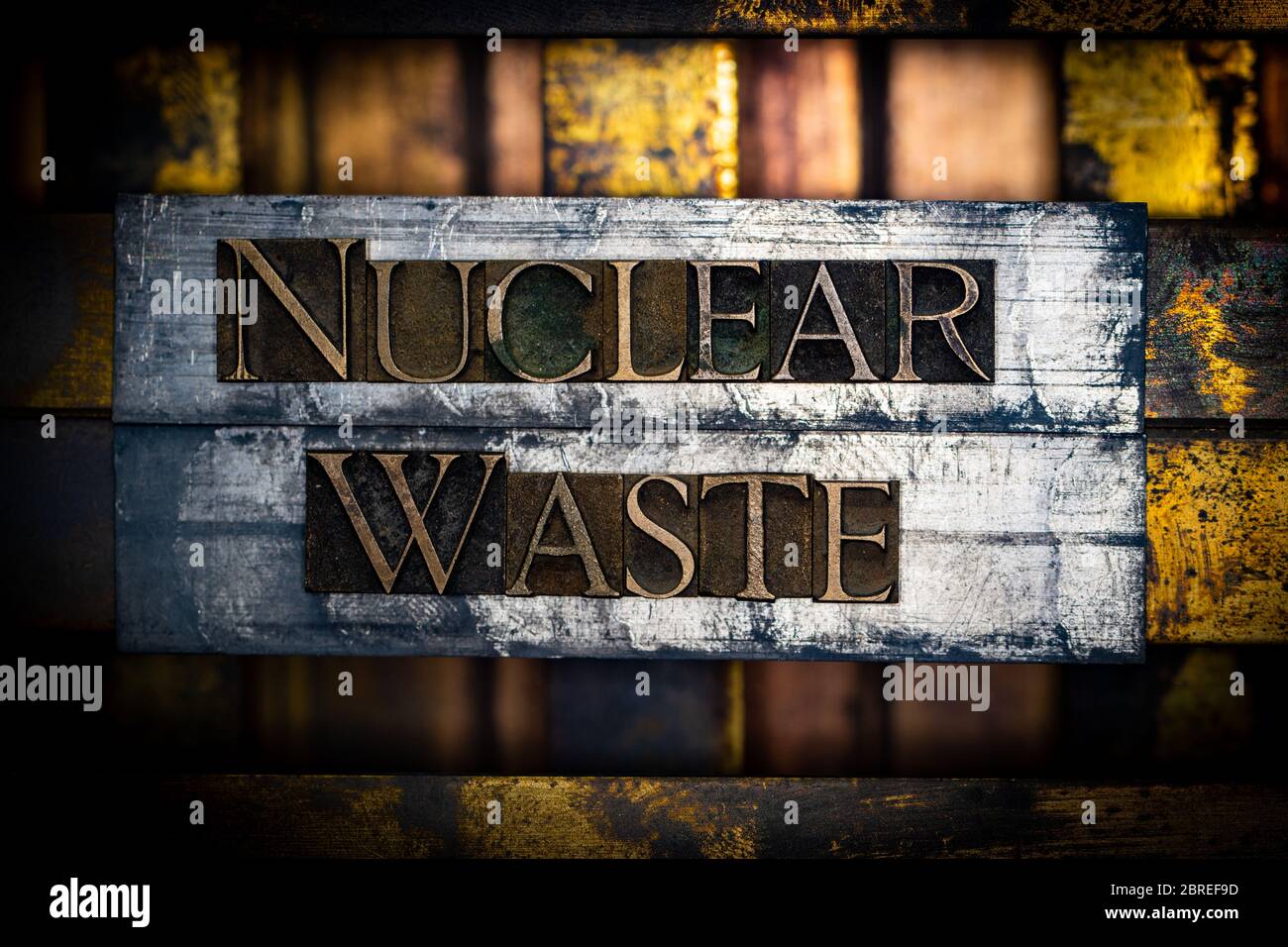 Photo of real authentic typeset letters forming Nuclear Waste text with on vintage textured silver grunge copper and gold layered background Stock Photo