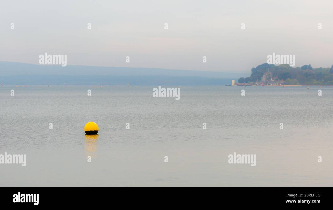 Landscape photograph overlooking part of Poole Harbour with yellow shallow water buoy in foreground and Brownsea island in background on foggy day. Stock Photo