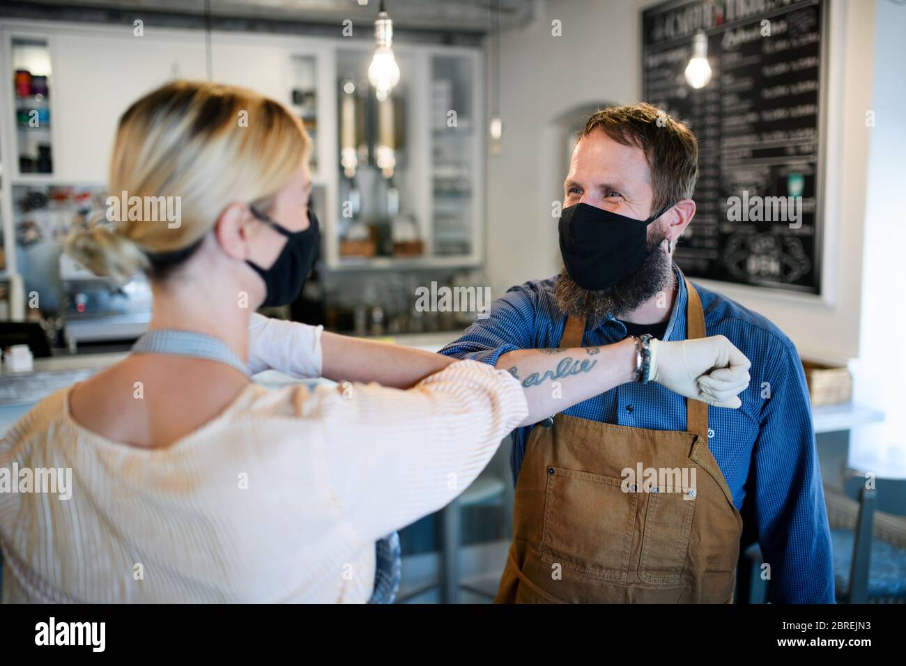 Coffee shop owners with face masks elbow bumping, open after lockdown