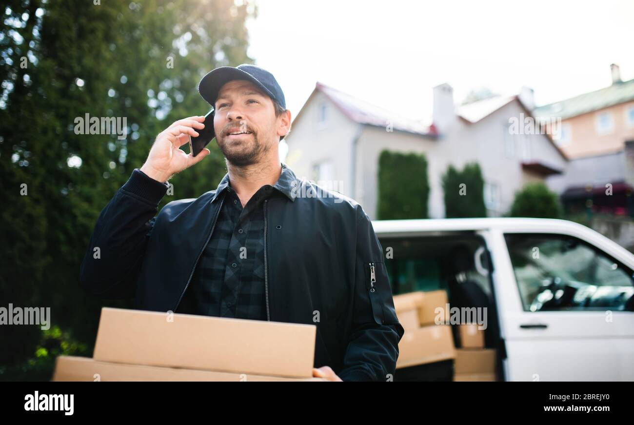 Delivery man courier delivering parcel box in town using smartphone. Stock Photo