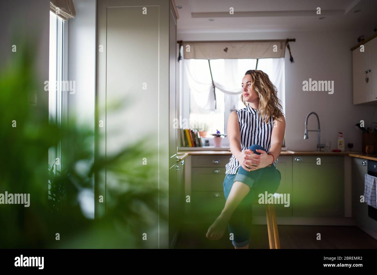 Young woman sitting in kitchen indoors at home, relaxing. Stock Photo